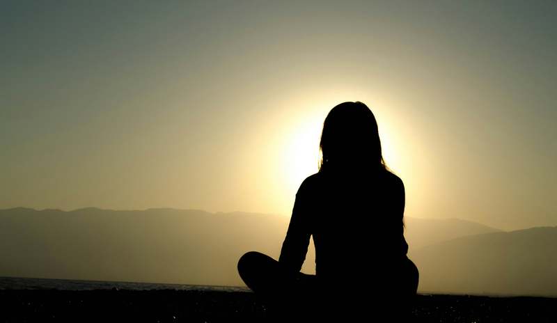 Friendly illustrated icon of a smiling person seated in lotus pose with a soft glow around their head, minimalist line art style